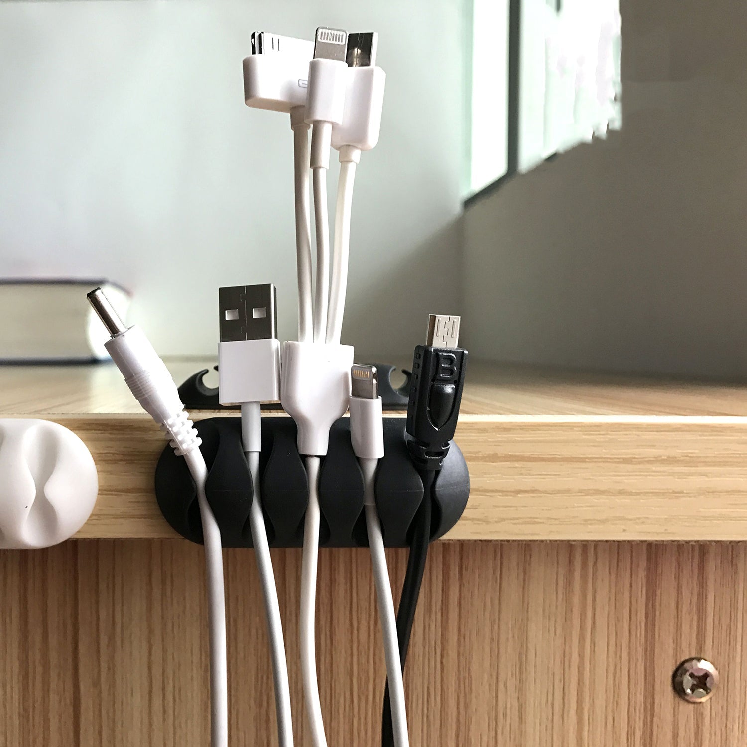 Cable organiser clips in black, shown holding multiple wires neatly on a desk.