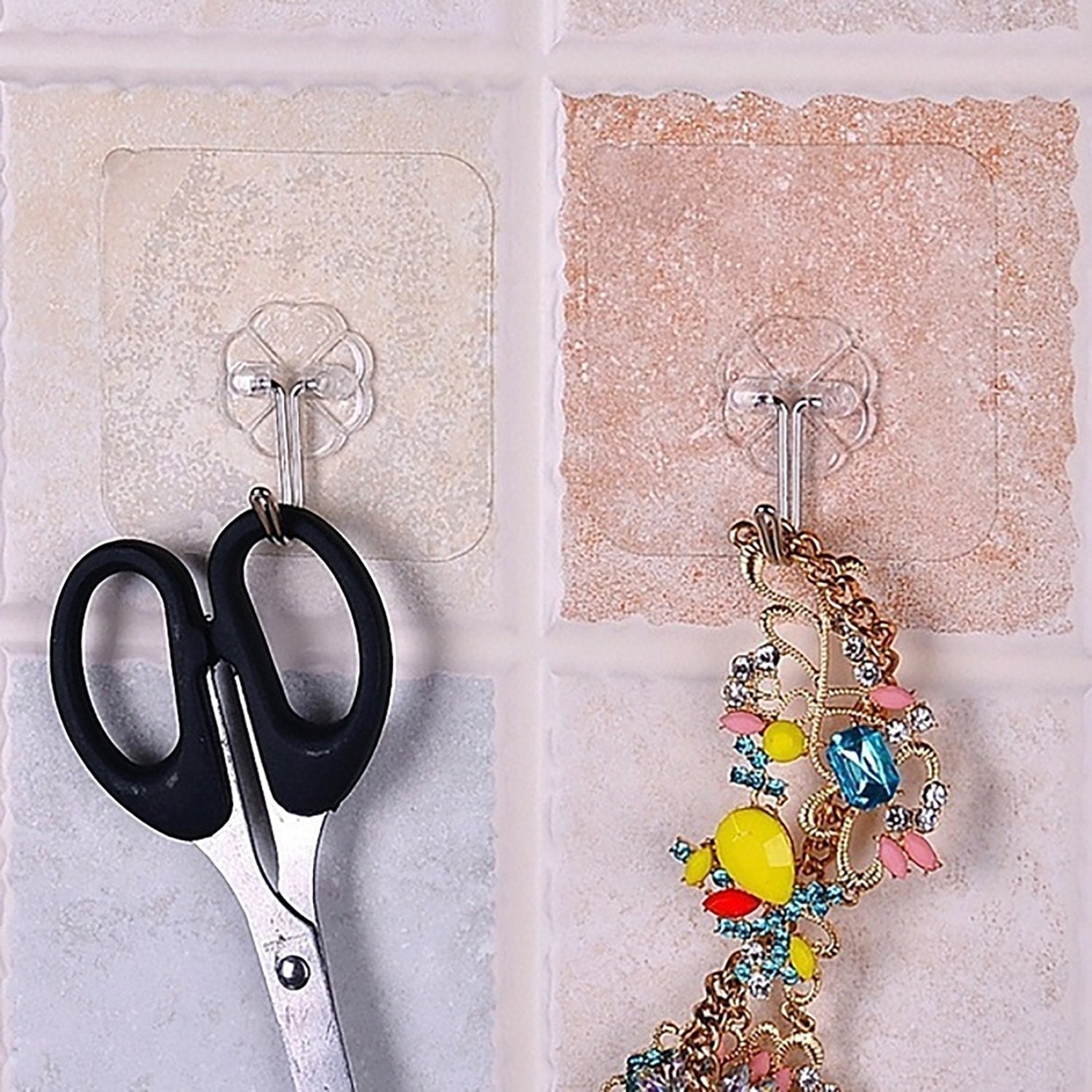 Pair of small stainless steel adhesive hooks on a white wall.