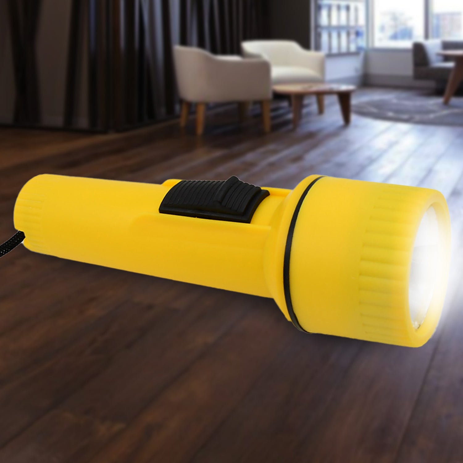 A yellow plastic torch with a black wrist strap rests on a wooden surface outdoors, surrounded by green foliage.